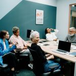 Grupo diverso de profissionais reunido em um escritório moderno, conversando e colaborando em torno de uma mesa.