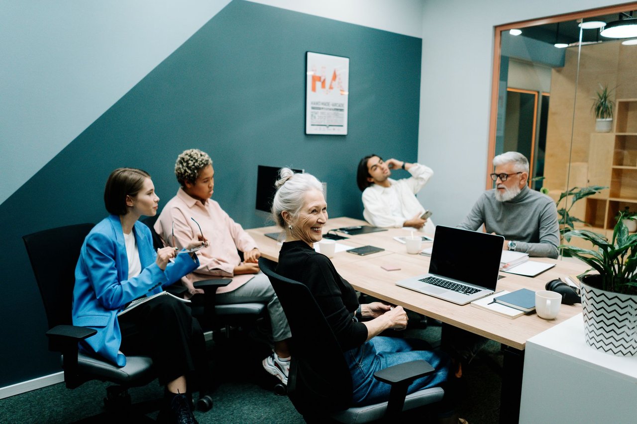 Grupo diverso de profissionais reunido em um escritório moderno, conversando e colaborando em torno de uma mesa.