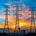 Torres de transmissão de alta tensão e linhas elétricas recortadas contra o céu ao entardecer.