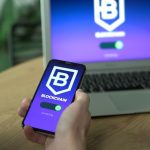 Pessoa utiliza um aplicativo de blockchain no smartphone, com a tela refletida em um laptop.