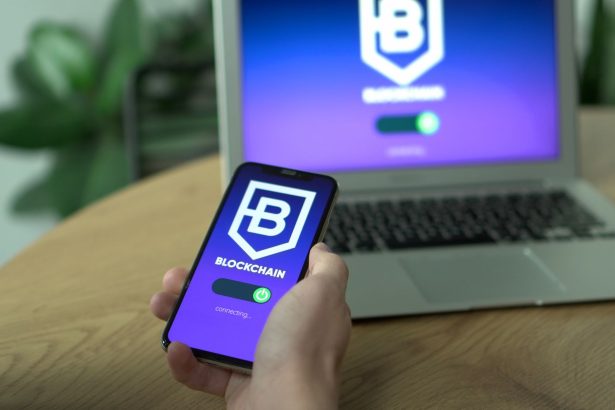 Pessoa utiliza um aplicativo de blockchain no smartphone, com a tela refletida em um laptop.