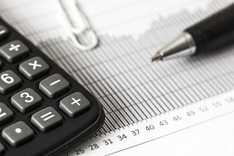 Calculadora, caneta e documentos financeiros sobre uma mesa, representando cálculos orçamentários e análise fiscal