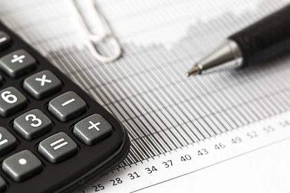 Calculadora, caneta e documentos financeiros sobre uma mesa, representando cálculos orçamentários e análise fiscal