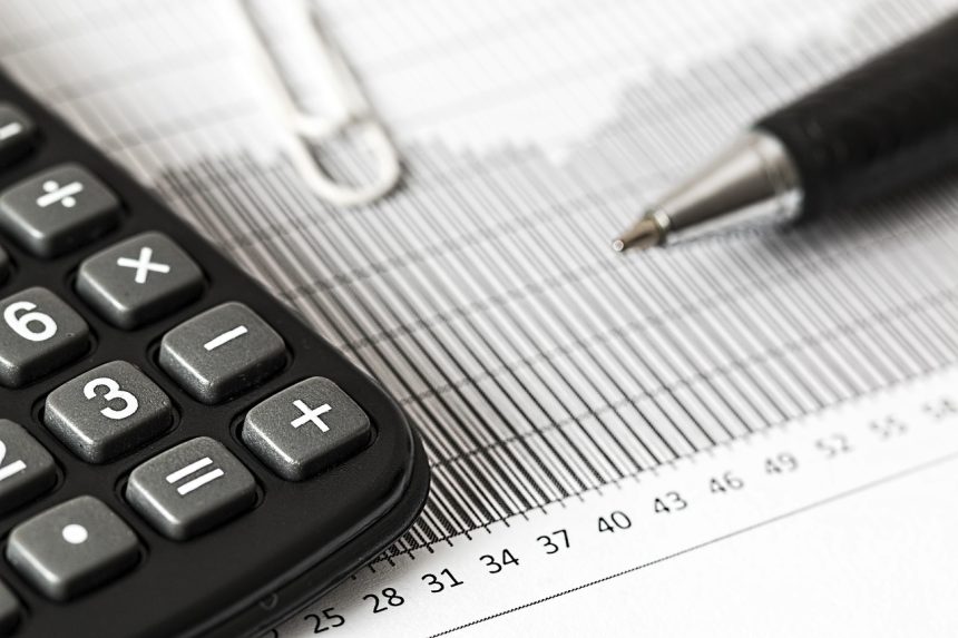 Calculadora, caneta e documentos financeiros sobre uma mesa, representando cálculos orçamentários e análise fiscal